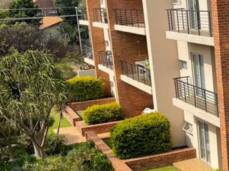 Exterior view of an apartment building featuring brick facade, multiple balconies with metal railings, and well-maintained landscaped garden areas.