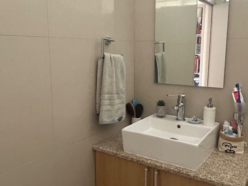 A compact bathroom featuring a modern vessel sink set on a granite-topped vanity cabinet with neutral wall tiling and a wall-mounted mirror.