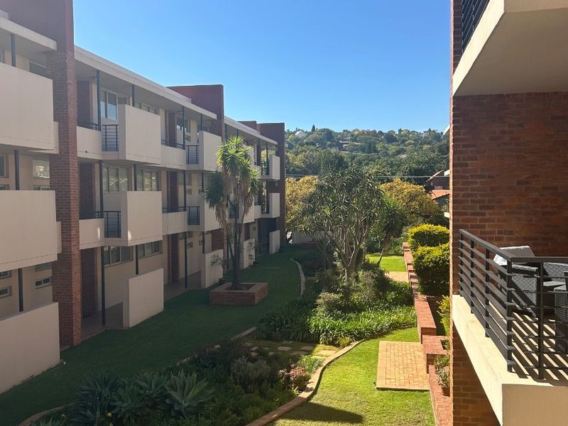 View of the apartment complex rear facade featuring brick architecture, private balconies, and a well-maintained communal garden area.