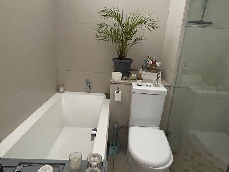 A modern bathroom featuring a built-in bathtub, a toilet, and a glass-enclosed shower with neutral wall and floor tiling.