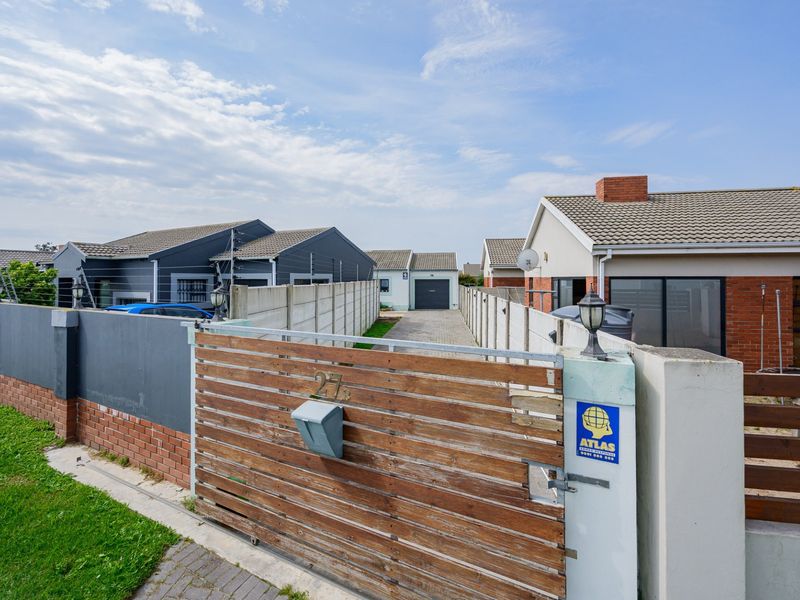 Front view of the property featuring a sliding timber gate, paved driveway, and secure boundary walls leading to the main residence.