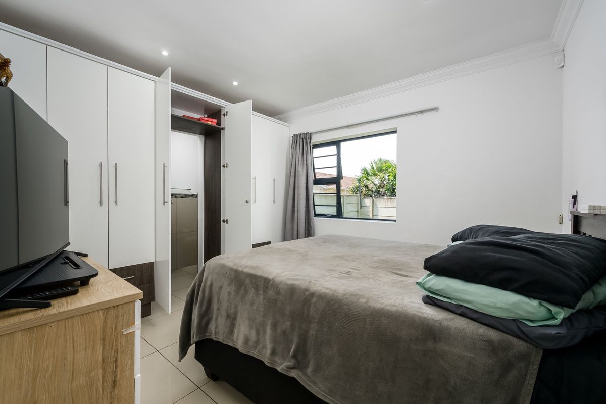 A well-maintained bedroom featuring built-in cupboards, tiled flooring, and recessed downlights, offering a clean and functional living space.