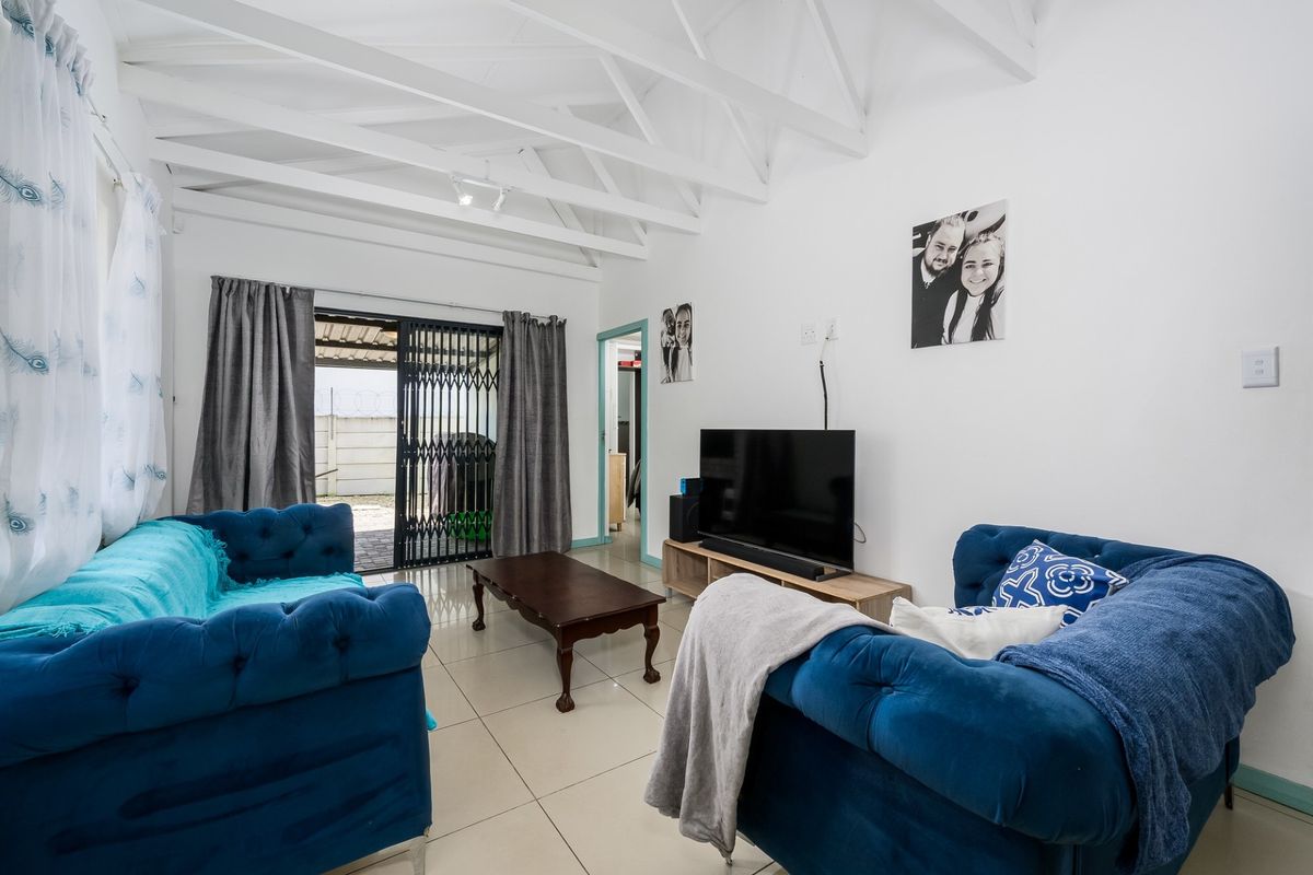 A bright living room featuring exposed white rafters, tiled flooring, and a sliding glass door providing access to the exterior.