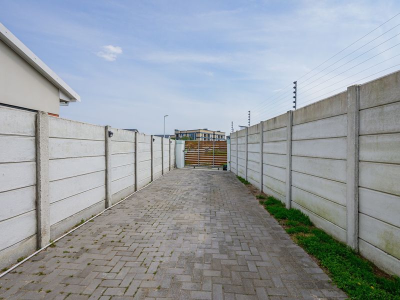 A paved driveway entrance featuring precast concrete boundary walls, electric fencing, and a secure sliding gate.