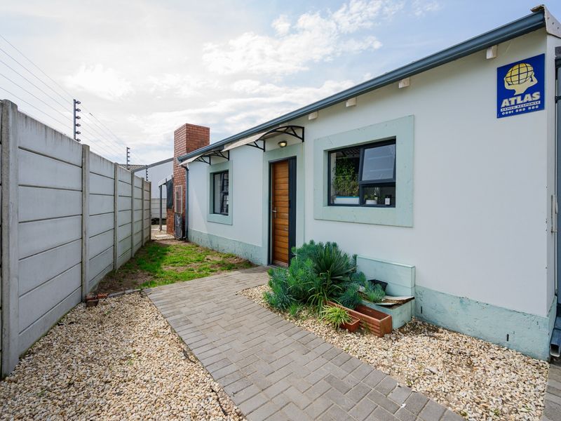 Rear exterior view of the property featuring a paved walkway, precast boundary wall with electric fencing, and a brick chimney.