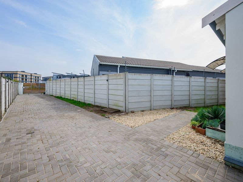 A paved rear exterior area featuring a precast concrete boundary wall with electric fencing and gravel landscaping.