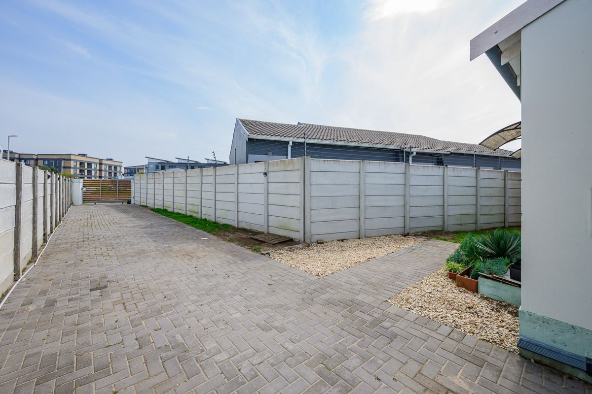 A paved rear exterior area featuring a precast concrete boundary wall with electric fencing and gravel landscaping.