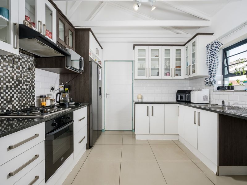 Modern kitchen featuring white and dark wood cabinetry, granite countertops, subway tile backsplash, gas hob, and exposed beam ceilings.
