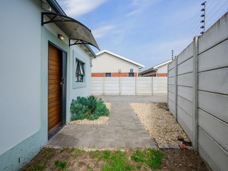 Rear exterior view featuring a paved walkway, precast concrete boundary wall with electric fencing, and a side entrance with a protective awning.