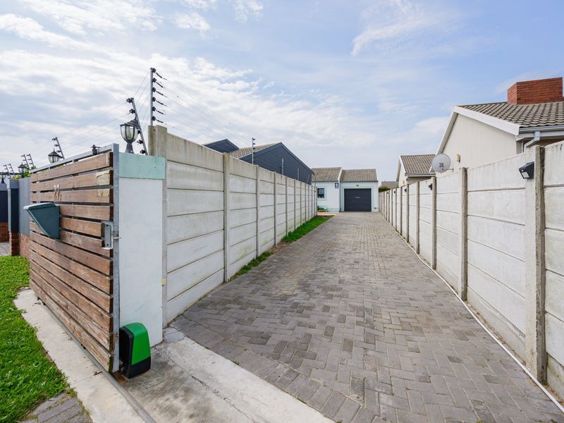 A paved driveway leading to a garage, enclosed by precast concrete boundary walls with integrated electric fencing and a sliding gate.