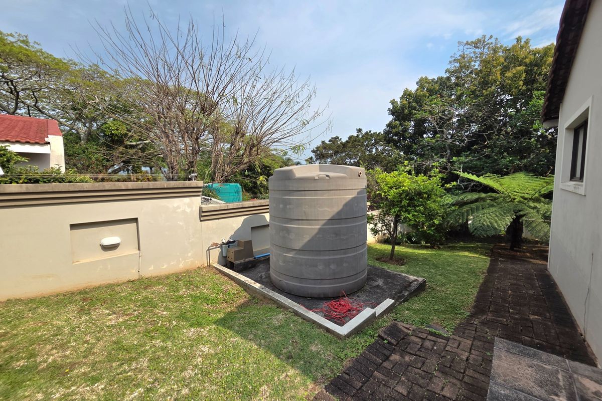 Rear garden area featuring a large water storage tank on a concrete plinth, adjacent to a boundary wall and paved walkway.