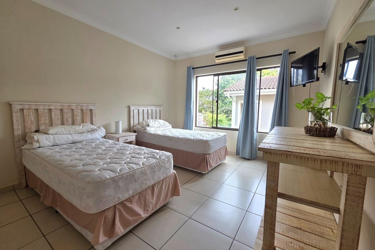 A spacious bedroom featuring tiled flooring, a wall-mounted air conditioning unit, and large sliding windows providing natural light.
