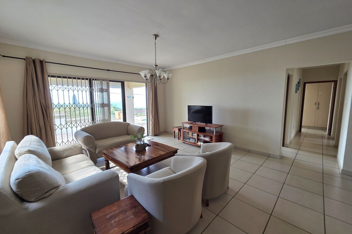 A spacious living room featuring tiled flooring, a coved ceiling, and a sliding glass door with a security gate leading to an outdoor area.