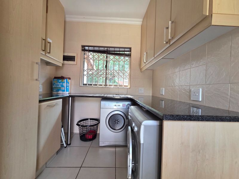 A functional laundry room featuring built-in light wood cabinetry, granite countertops, tiled backsplash, and tiled flooring with space for appliances.