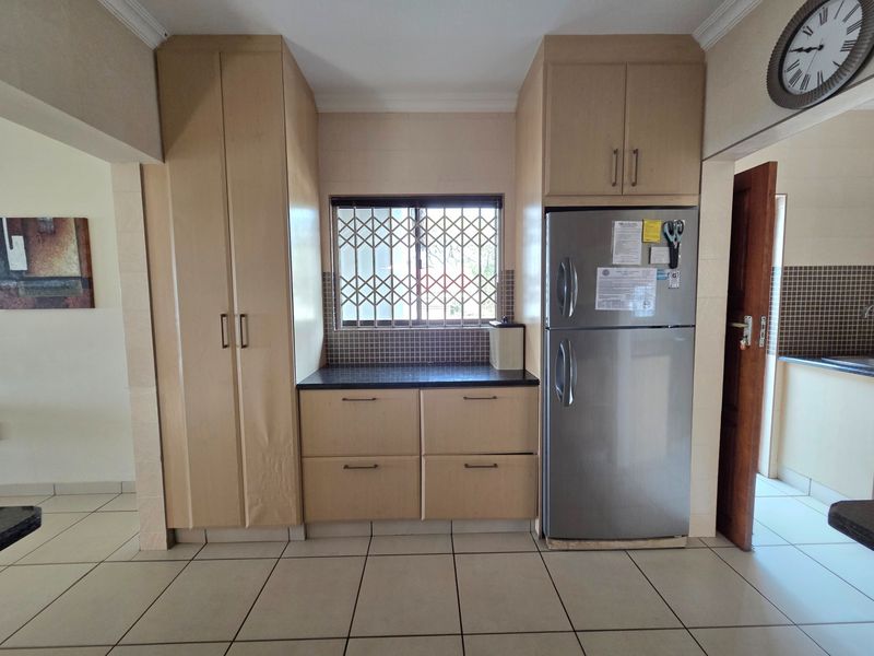 Kitchen area featuring light wood-tone built-in cabinetry, dark laminate countertops, tiled backsplash, and tiled flooring with a window security gate.