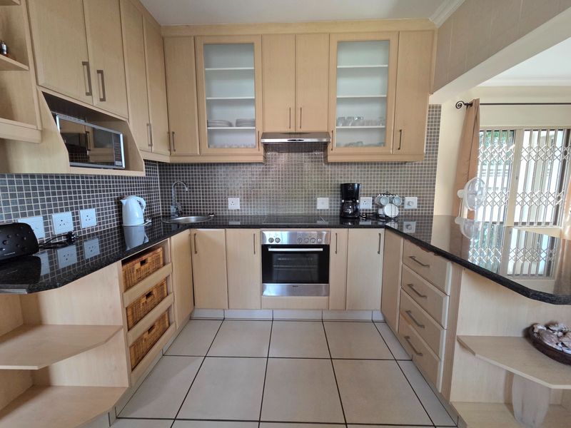 A well-maintained kitchen featuring light wood cabinetry, granite countertops, a mosaic tile backsplash, and integrated stainless steel appliances.