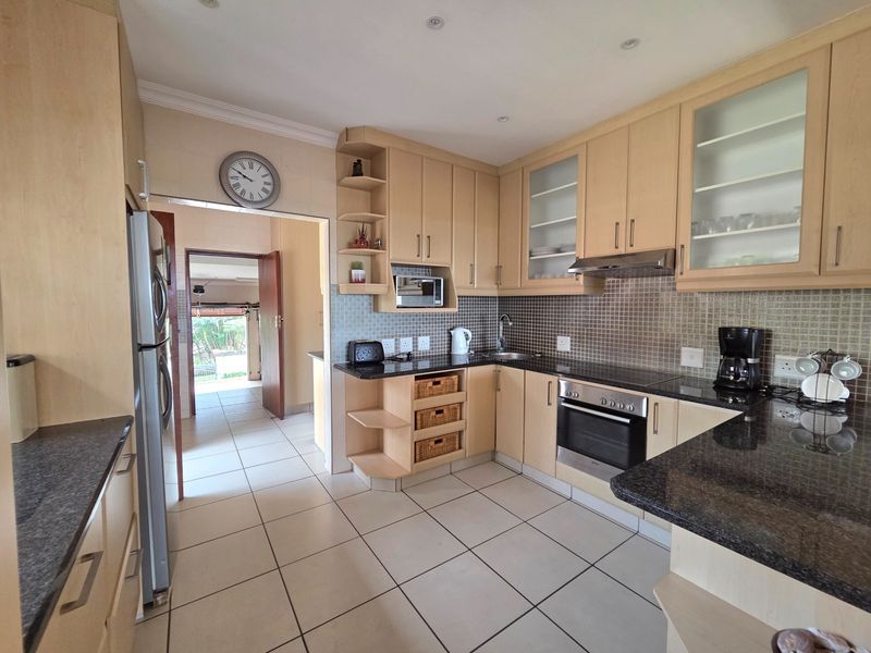 A functional kitchen featuring light wood cabinetry, granite countertops, mosaic tile backsplash, and built-in appliances, with tiled flooring throughout.