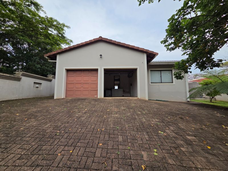 Front view of a residential property featuring a double garage with one closed door and a paved driveway.