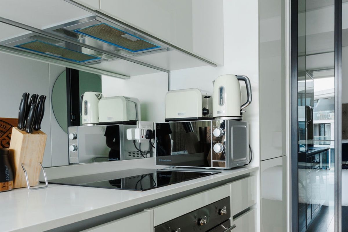 Modern kitchen featuring sleek white cabinetry, a mirrored splashback, integrated electric hob, and built-in oven, offering a clean and contemporary aesthetic.