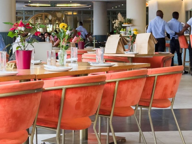 A spacious open-plan dining area featuring tiled flooring, structural columns, and modern recessed ceiling lighting, suitable for a commercial or apartment complex setting.