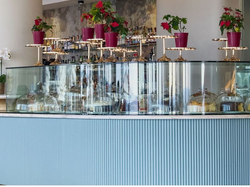 A modern, stylish bar area featuring a curved counter with blue fluted paneling, a glass display case, and integrated back shelving.
