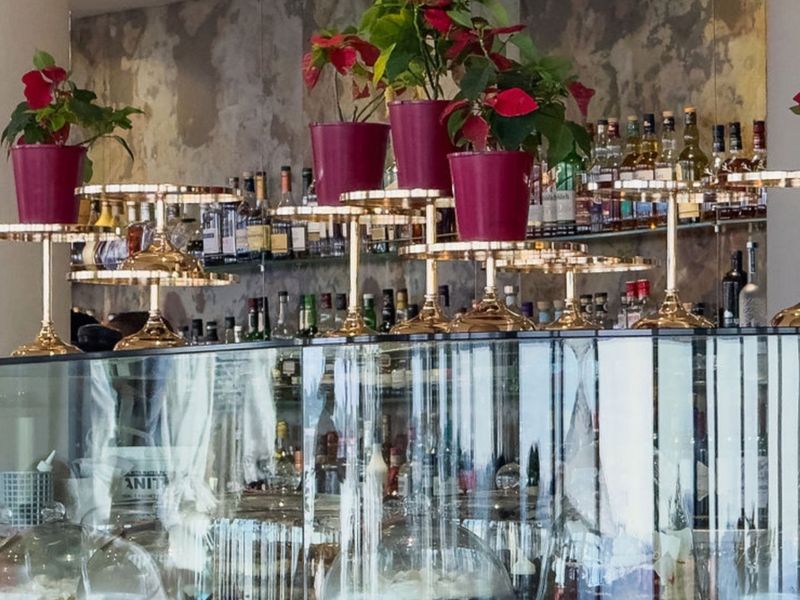 A modern bar area featuring a glass display counter and a mirrored back wall with glass shelving for beverage storage.