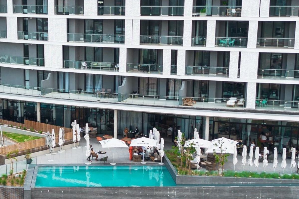 Elevated view of a modern apartment complex featuring a swimming pool, paved terrace area, and multiple balconies with glass balustrades.