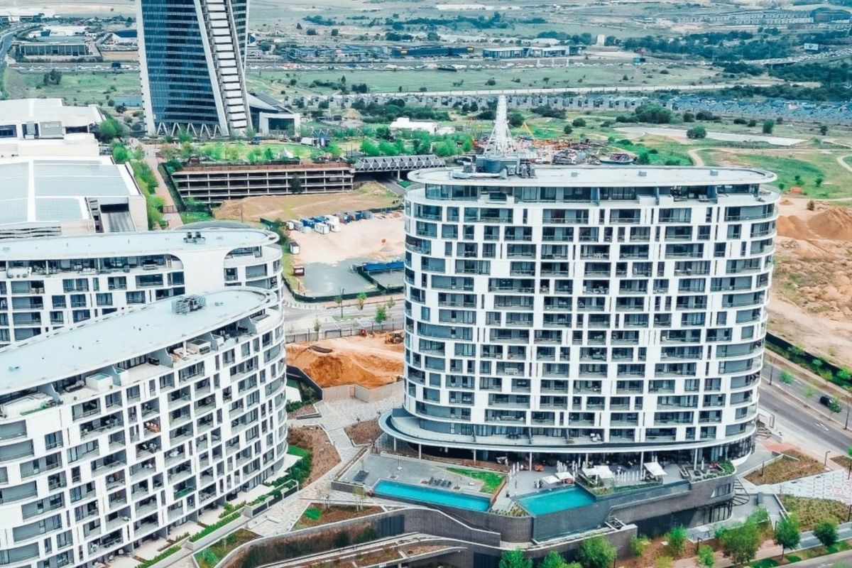 Aerial view of a modern apartment complex featuring high-rise residential towers, swimming pools, and landscaped outdoor areas in an urban setting.