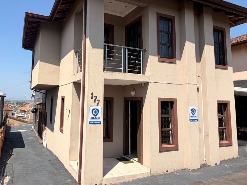 A two-story residential property featuring a balcony with stainless steel balustrades, security bars on windows, and a paved driveway entrance.