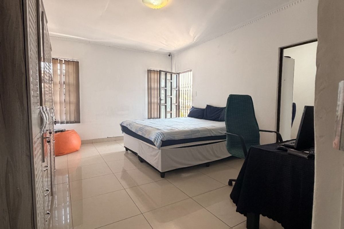 Spacious bedroom featuring large format floor tiles, built-in cupboards, and a ceiling access hatch, offering a functional layout with neutral finishes.