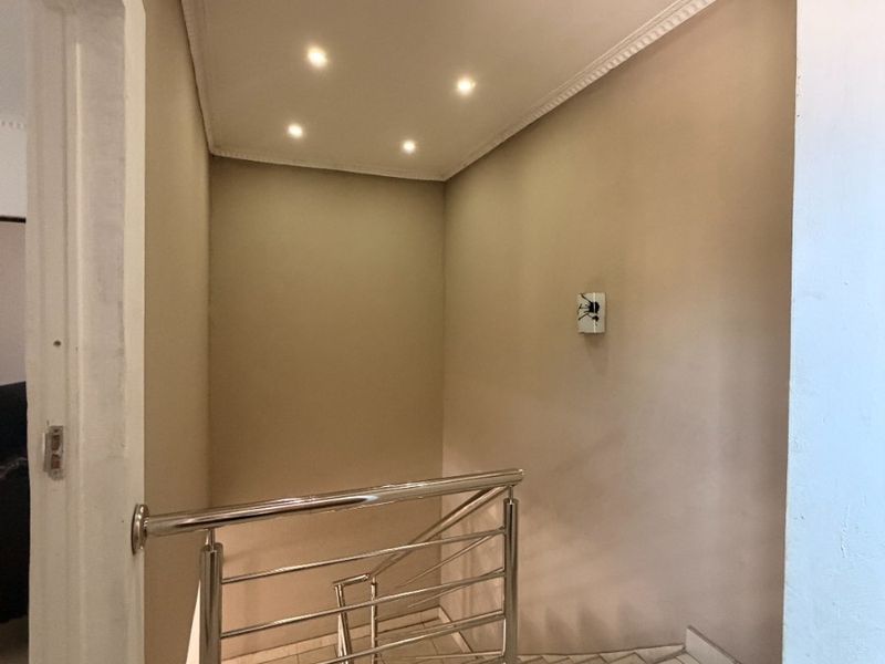 A clean, well-lit hallway featuring tiled flooring, recessed downlighting, and a modern stainless steel balustrade overlooking the staircase.