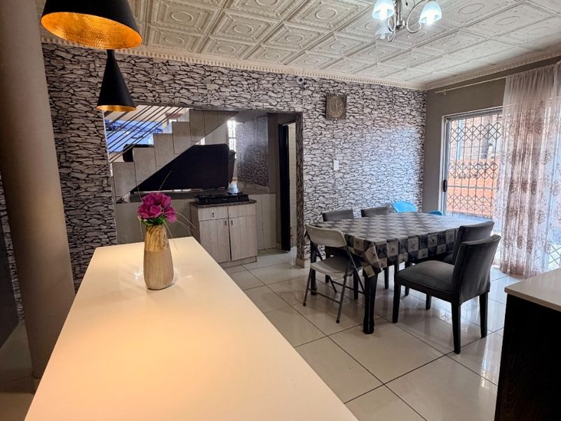 Open-plan living and dining area featuring tiled floors, a decorative coffered ceiling, stone-effect wall cladding, and a central kitchen island.