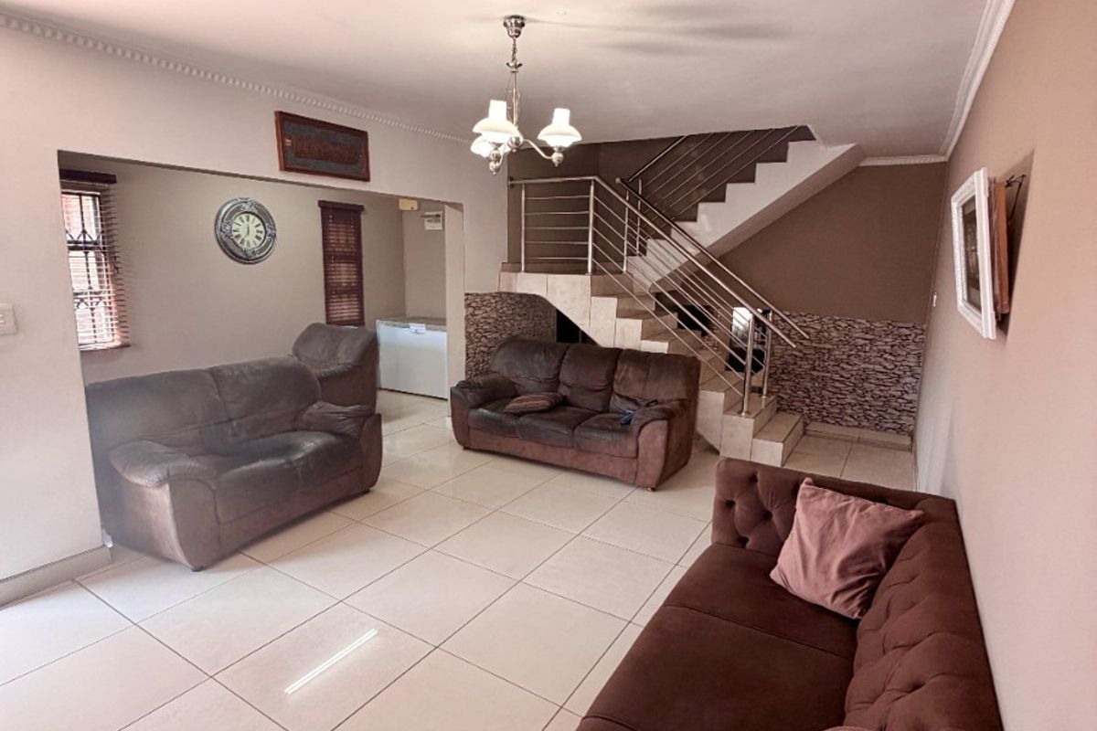 Spacious living area featuring large format floor tiles, a staircase with stainless steel balustrades, and decorative stone wall accents.