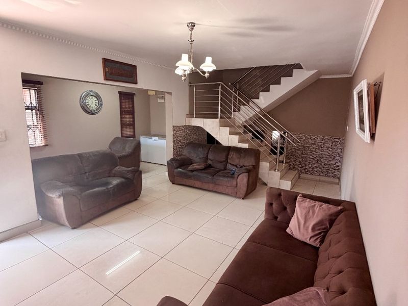 Spacious living area featuring large format floor tiles, a staircase with stainless steel balustrades, and decorative stone wall accents.