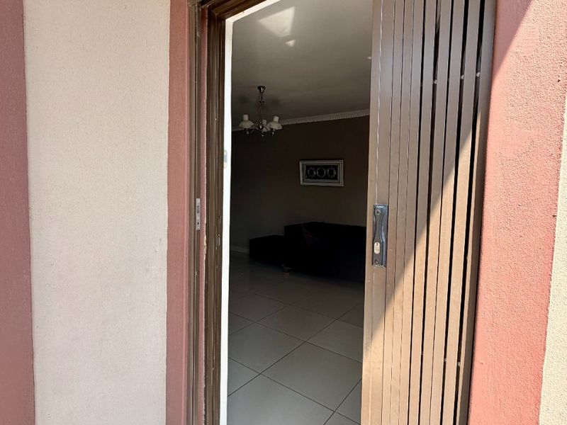 View through an open security gate into a tiled interior living space with a central ceiling light fixture.