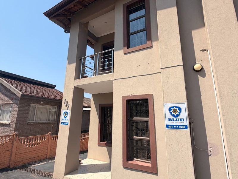 Front elevation of a two-story residential property featuring a covered entrance, upper-level balcony with stainless steel balustrade, and security window bars.