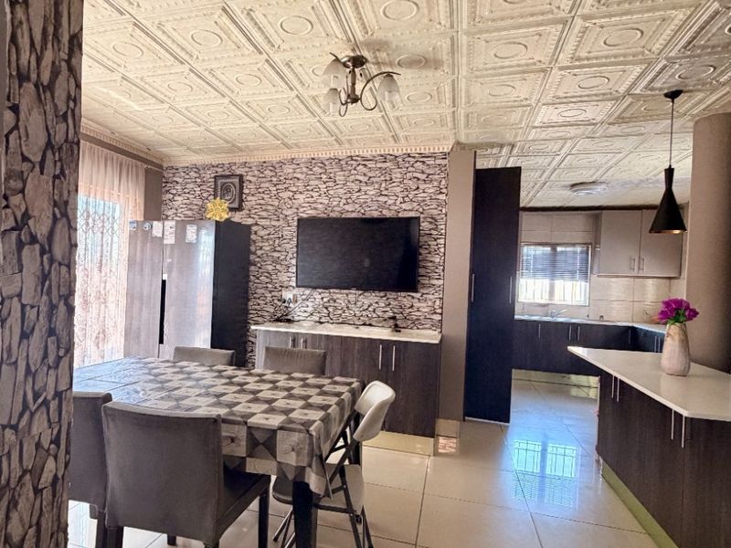 Open-plan living and kitchen area featuring tiled flooring, decorative coffered ceilings, and built-in cabinetry with stone-effect wall accents.