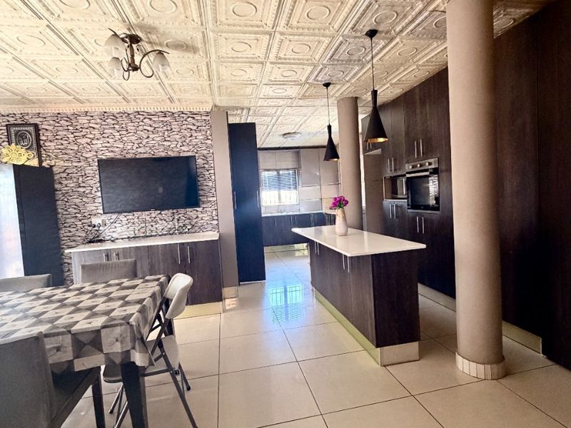 Open-plan living and kitchen area featuring a central island, built-in oven, tiled flooring, and decorative ceiling panels.