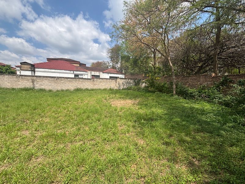 A vacant residential plot featuring a grassed area enclosed by a perimeter brick wall and mature trees.