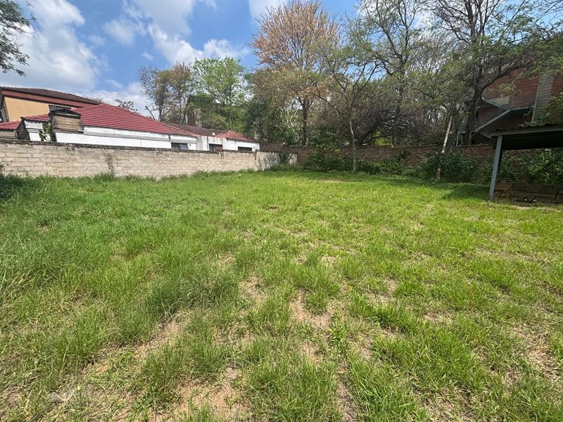 A spacious, level residential plot featuring a grass lawn, mature trees, and established perimeter boundary walls.