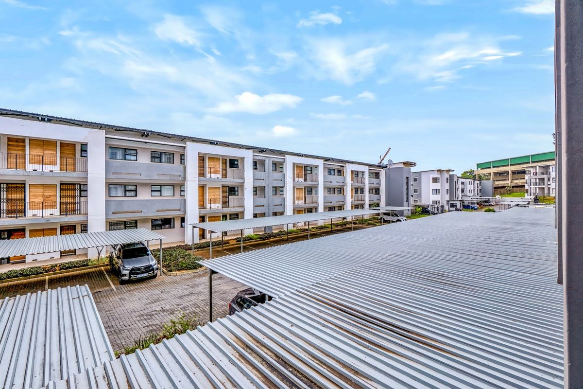 Exterior view of the apartment complex featuring covered parking bays, paved driveways, and multiple levels of residential units with balconies.