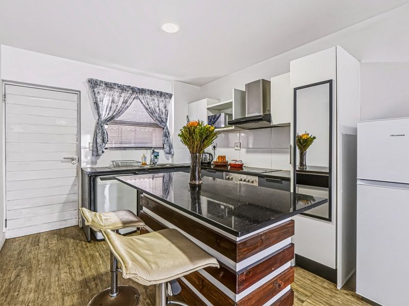 Modern kitchen featuring dark granite countertops, white cabinetry, built-in hob and oven, extractor fan, and durable laminate flooring.