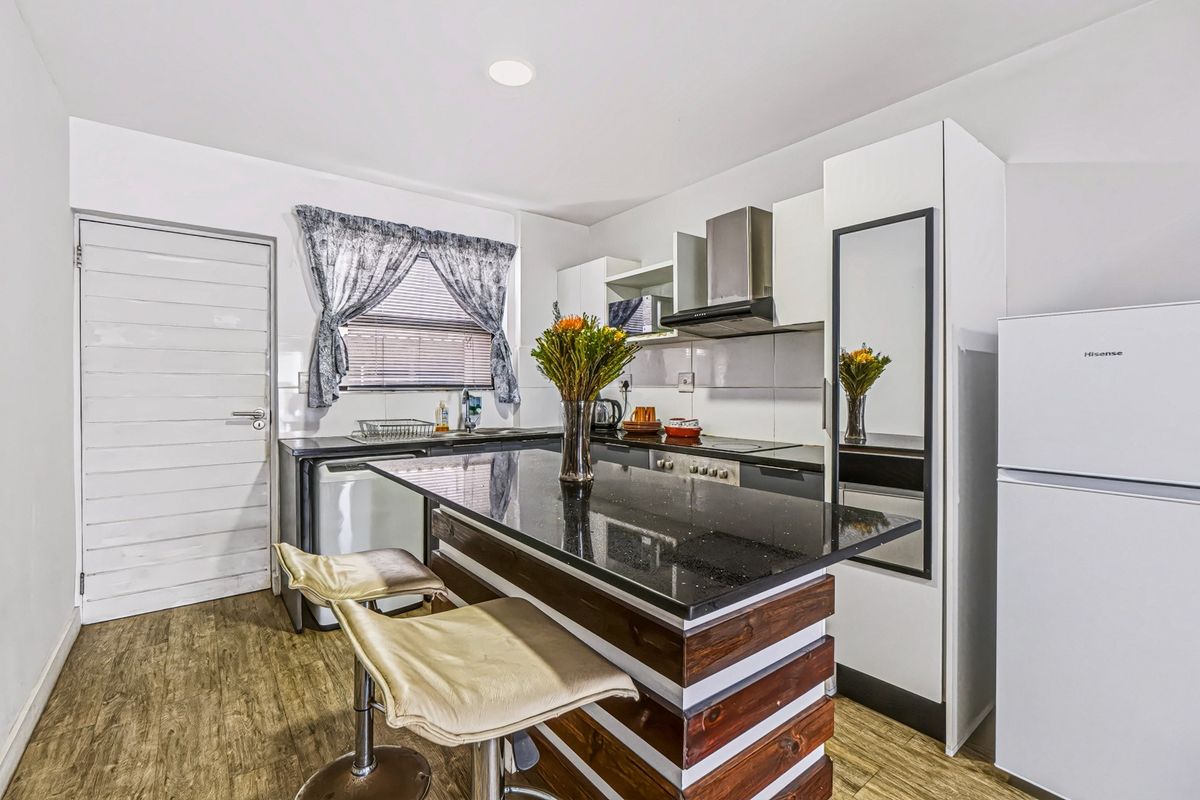 Modern kitchen featuring dark granite countertops, white cabinetry, built-in hob and oven, extractor fan, and durable laminate flooring.