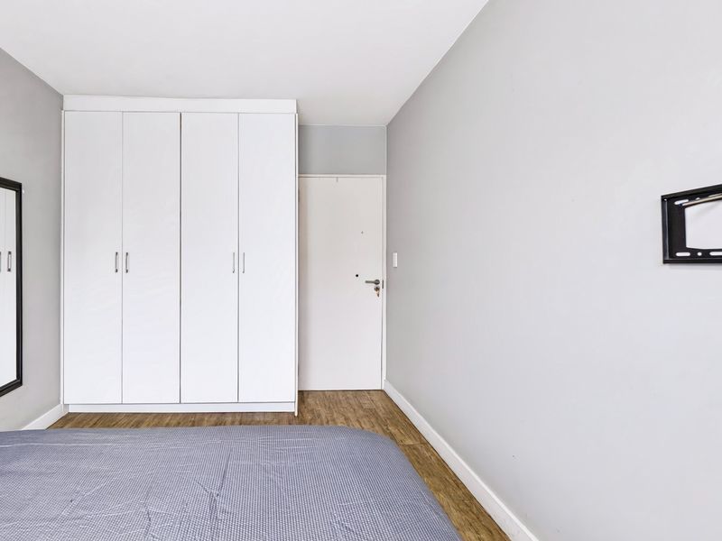 A clean, neutral bedroom featuring light grey walls, wood-look laminate flooring, and a large white built-in wardrobe.