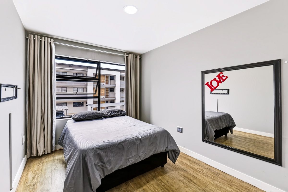 A well-maintained bedroom featuring laminate flooring, recessed ceiling lighting, and a large window with neutral curtains.