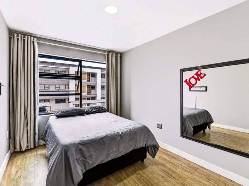 A well-maintained bedroom featuring laminate flooring, recessed ceiling lighting, and a large window with neutral curtains.