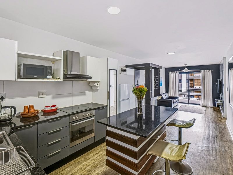 Modern open-plan kitchen and living area featuring sleek cabinetry, granite countertops, a central island, and direct access to a private balcony.