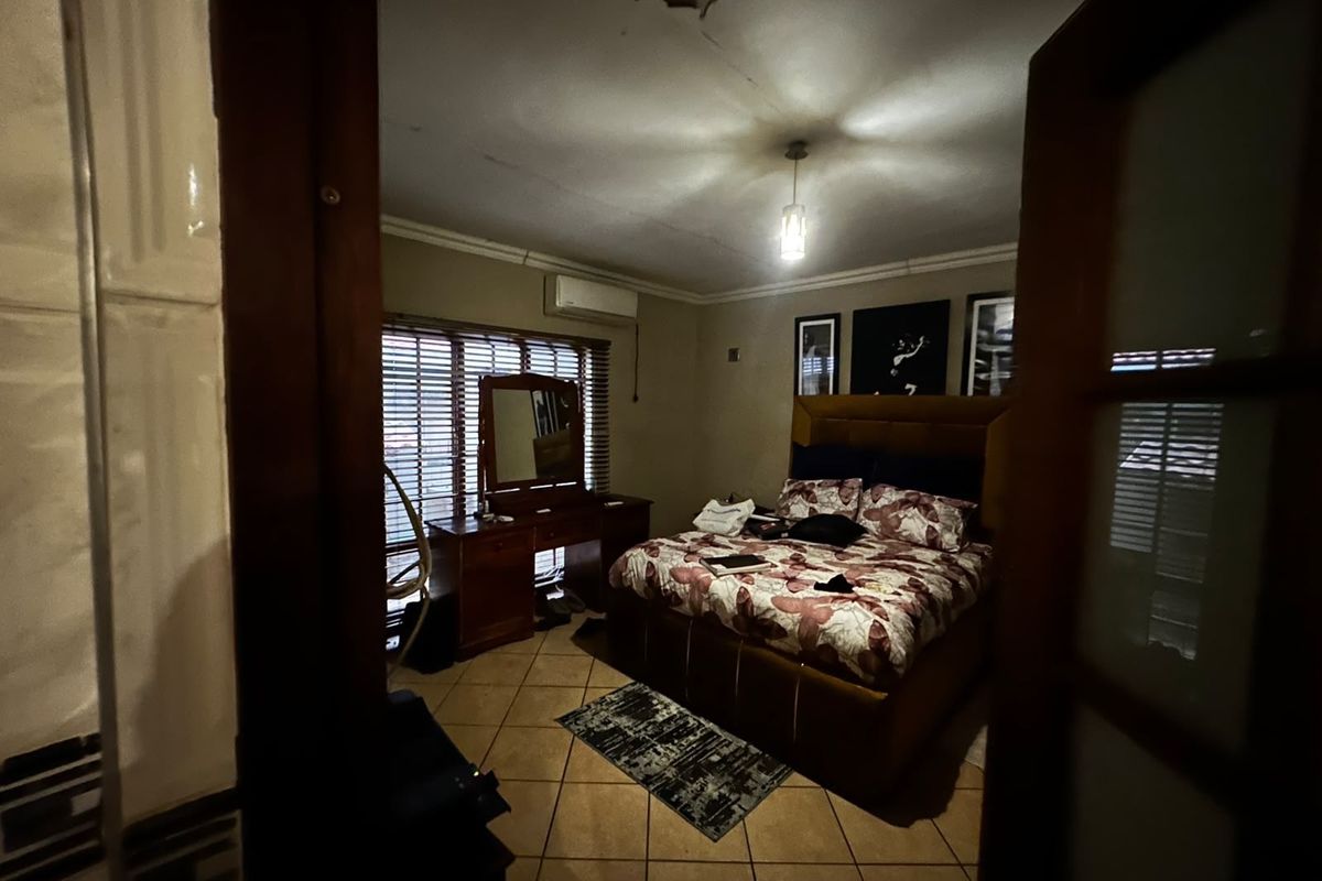 A bedroom featuring tiled flooring, a split-system air conditioner, and venetian blinds, showing signs of ceiling damage requiring repair.