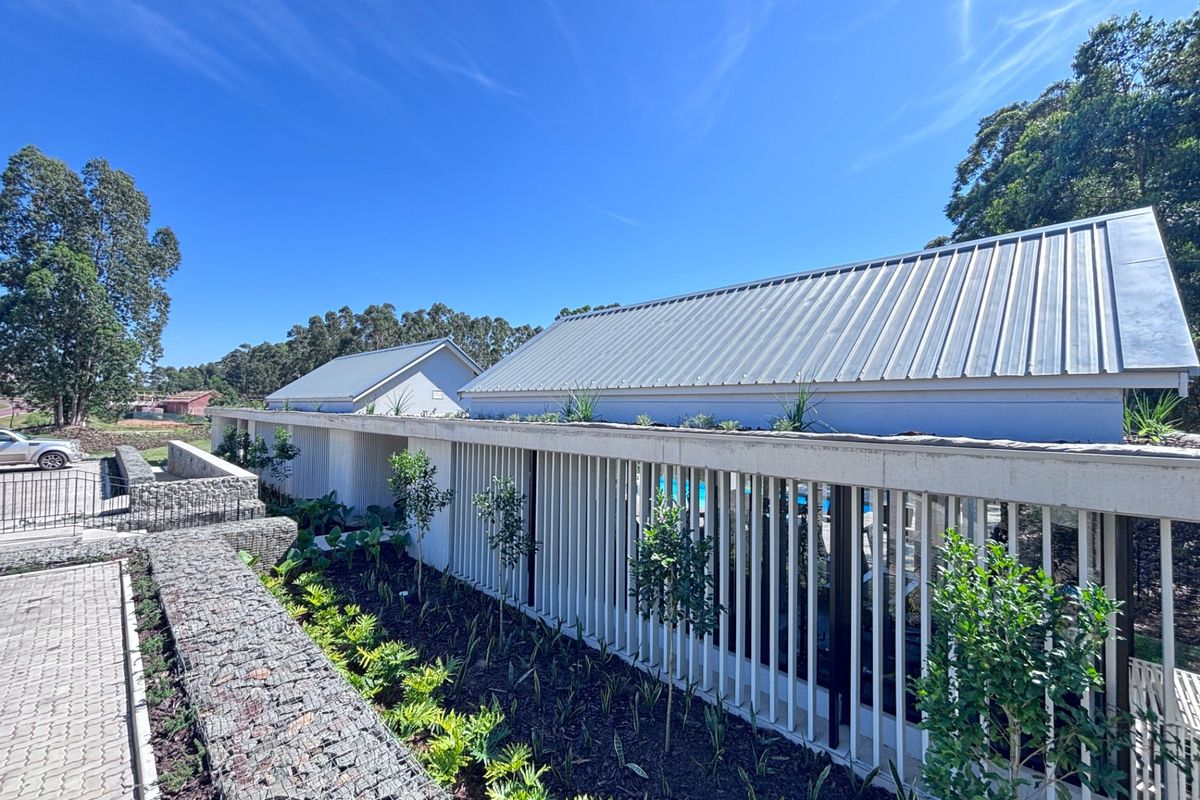 Exterior view of a modern apartment complex featuring gabion retaining walls, metal roofing, and vertical slat privacy screening with landscaped garden beds.