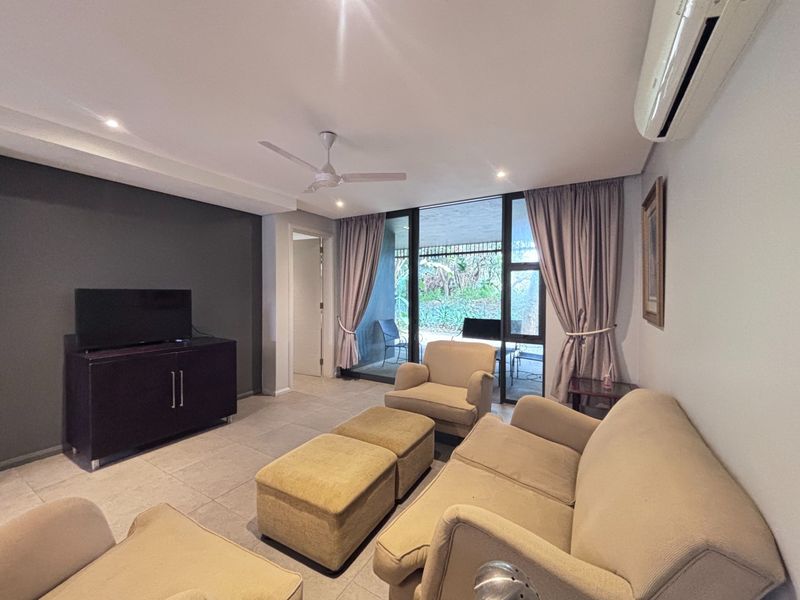 A comfortable living room featuring tiled flooring, a ceiling fan, split-system air conditioning, and large sliding glass doors providing access to the patio.